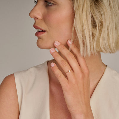 14k Goud ring met kleine diamant aan vrouwelijk hand met korte blonde haren.