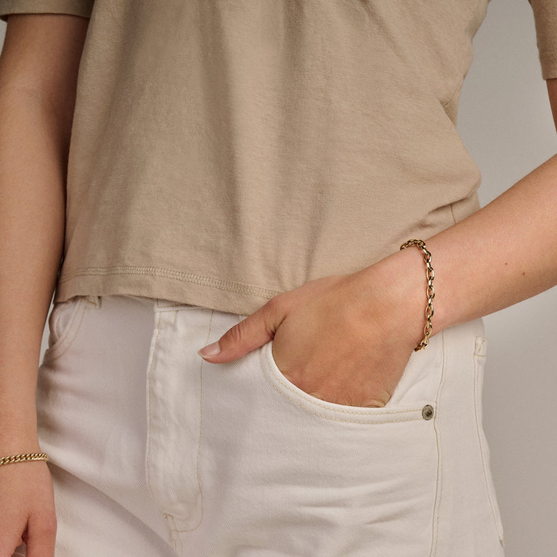 14k goud armband met grove schakels gedragen bij beige top en witte broek.
