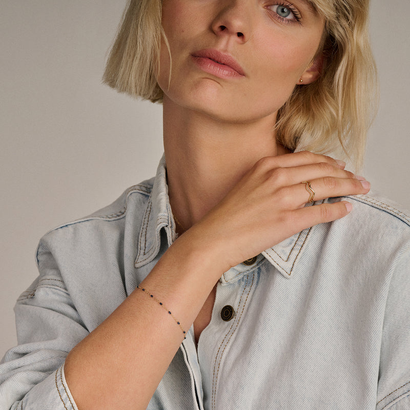 14k goud armband met fijne schakels en blauwe resin accenten gedragen aan pols.