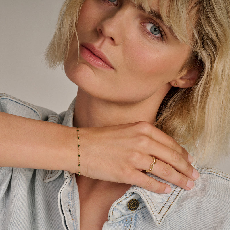 Bracelet en or 14k à maillons fins et perles en résine verte au poignet d'une femme.