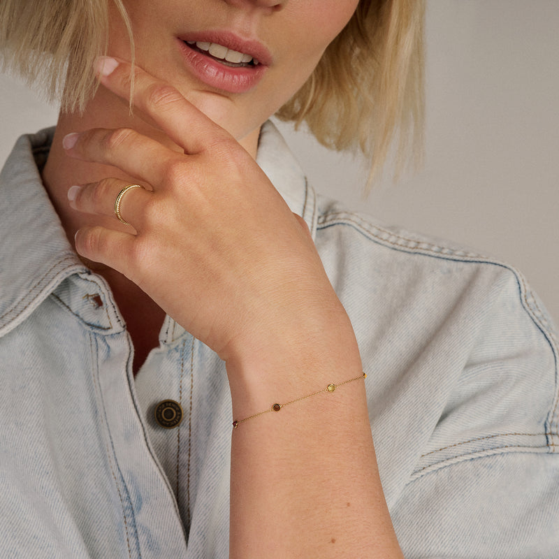 Fijne 14k goud armband met kleine gekleurde stenen aan slanke pols.