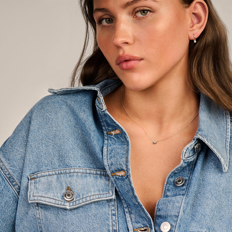 Bicolor ketting met 14k wit en geel goud en kleine zirkonia hanger bij een vrouw in spijkerjas.