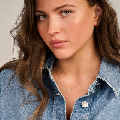 Delicate ketting van 14k geel goud met kleine zirkonia hanger gedragen bij een denim blouse.