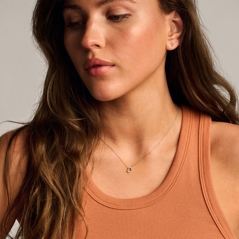 Collier en or blanc 14k avec petit cœur et zircone étincelante, porté avec des cheveux foncés.