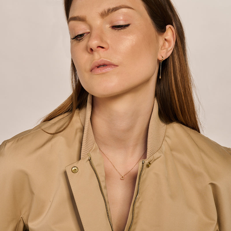 14k Goud fijne schakelketting met subtiel hartje, gedragen door vrouw in beige jas.