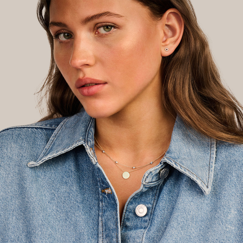Dunne ketting van 14k geelgoud met kleine zirkonia hanger, gedragen met blauwe denim blouse.