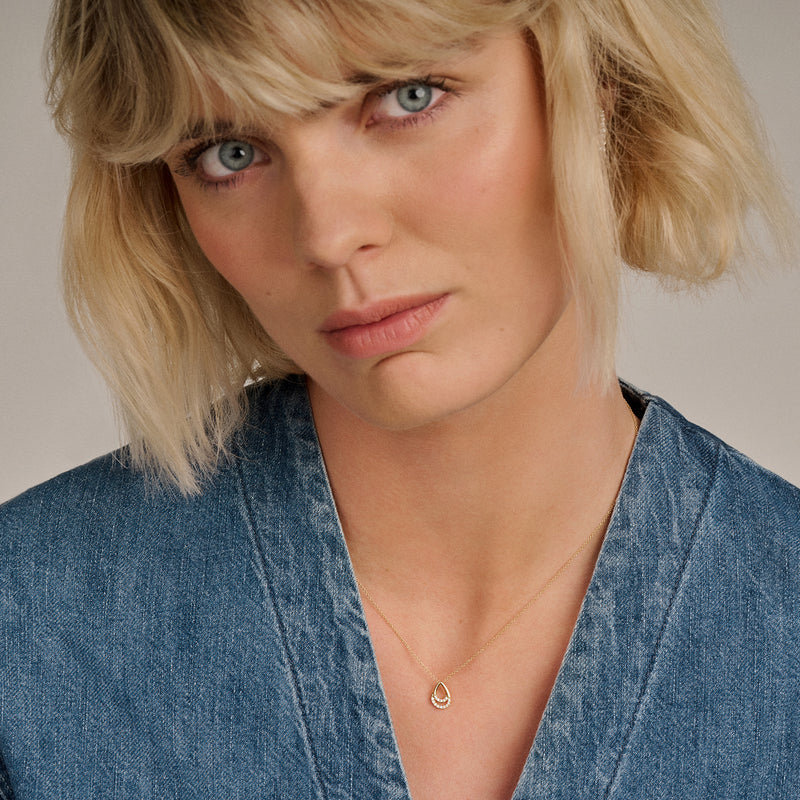 14k goud ketting met fijne schakels en zirkonia hanger gedragen bij een denim blouse.