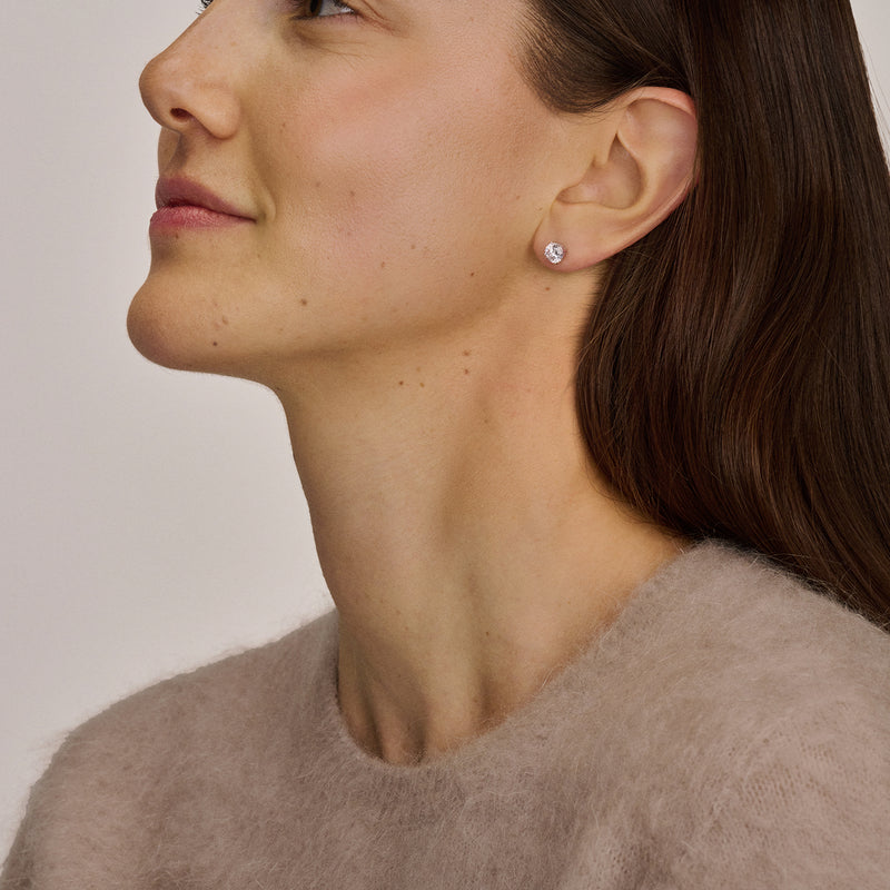 Oorknop van 14k wit goud met glinsterende zirkonia in oor van vrouw met beige trui.