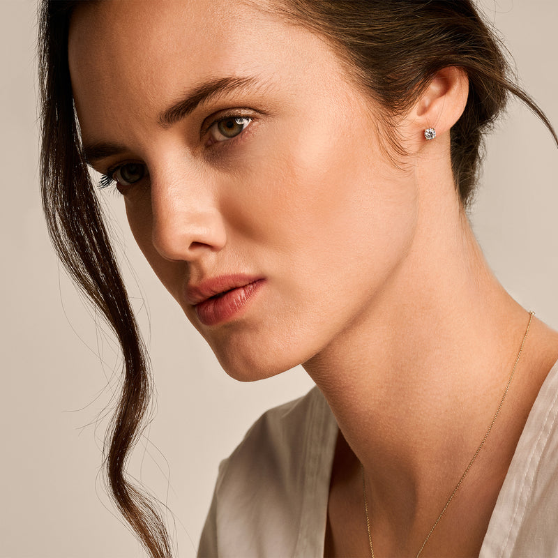 Puces d'oreilles en or jaune 14k avec pierre de Zircone étincelante, brillance subtile, gros plan sur une femme.