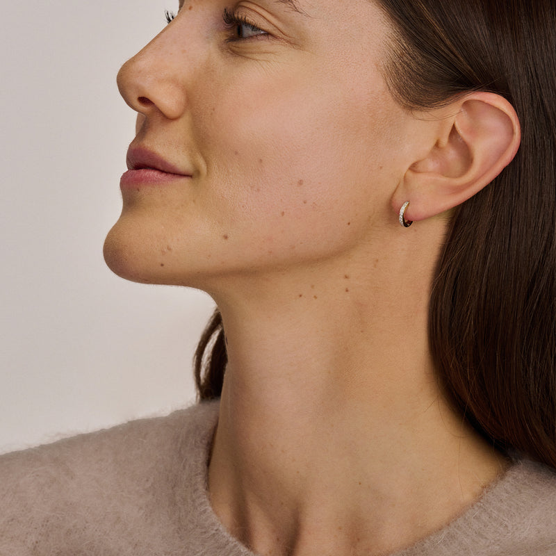 Bicolor oorring van 14k wit en rosé goud met zirkonia, gedragen aan oor van vrouw.