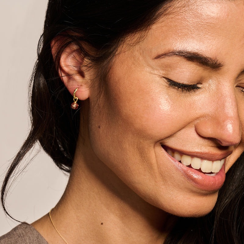 Oorring van 14k goud met kleine groene edelsteen, zichtbaar aan linkeroor.