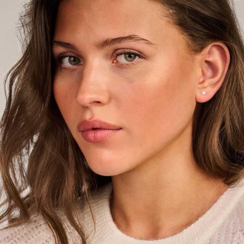 Puces d'oreilles avec perle d'eau douce en or jaune 14k, portées à l'oreille d'une femme.