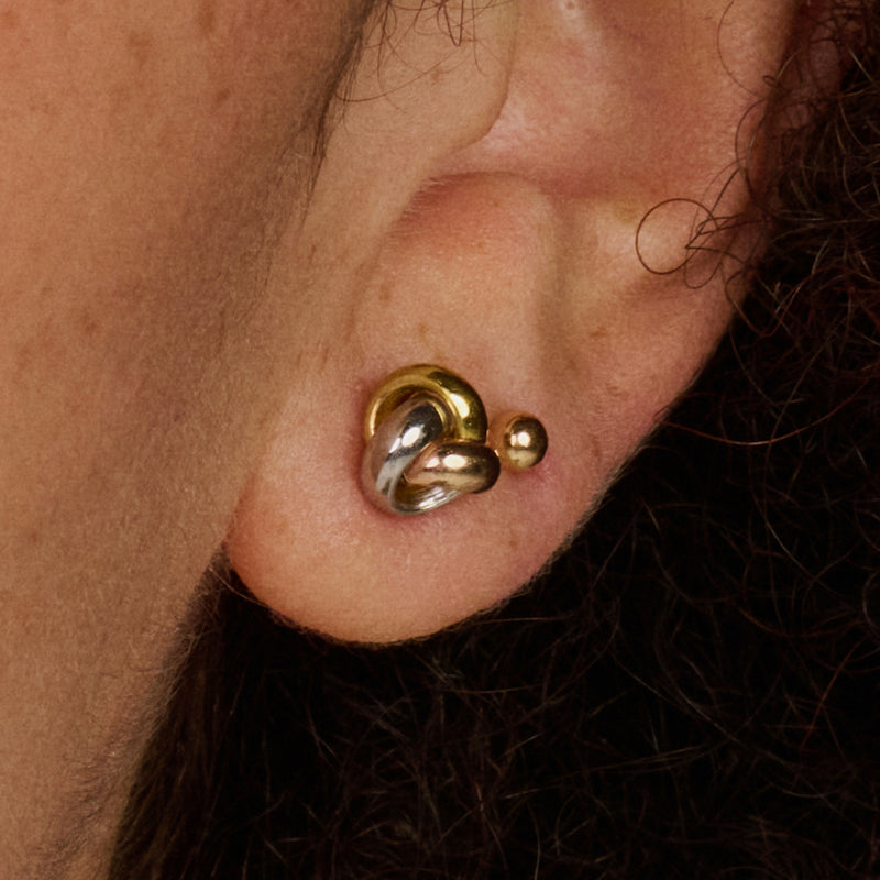 Bicolor 14k goud oorbel knopje met vloeiende vormen, gedragen in oorlel.