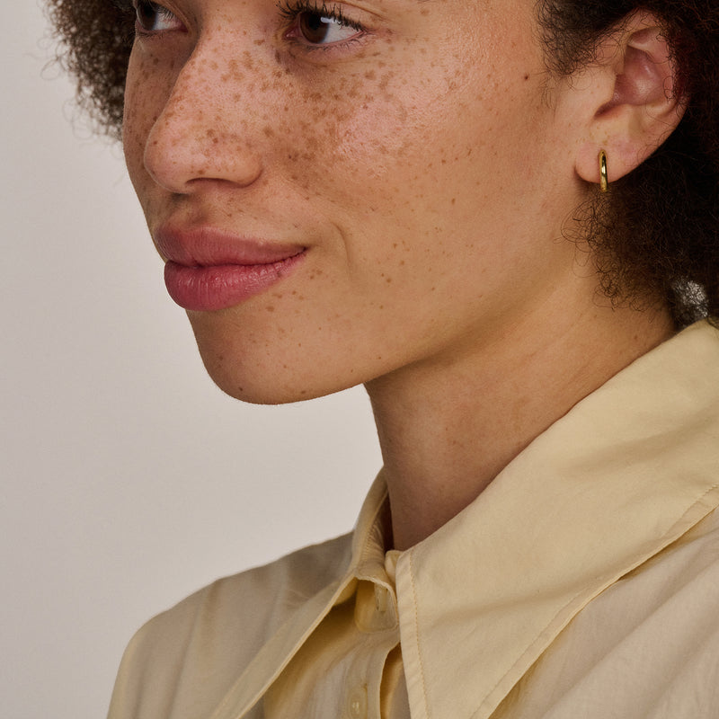 Oorring in 14k geel goud met gladde, glanzende afwerking, gedragen aan oorlel.