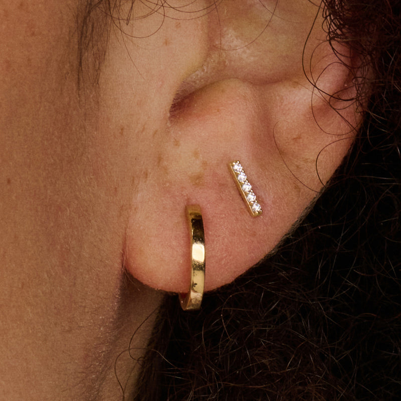 Oorknopje staafje met drie zirkonia in glanzend 14k goud, close-up oor.