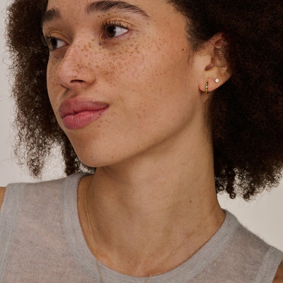 Oorknopje van 14k geelgoud met kleine heldere zirkonia steen, bicolor goud detail zichtbaar.