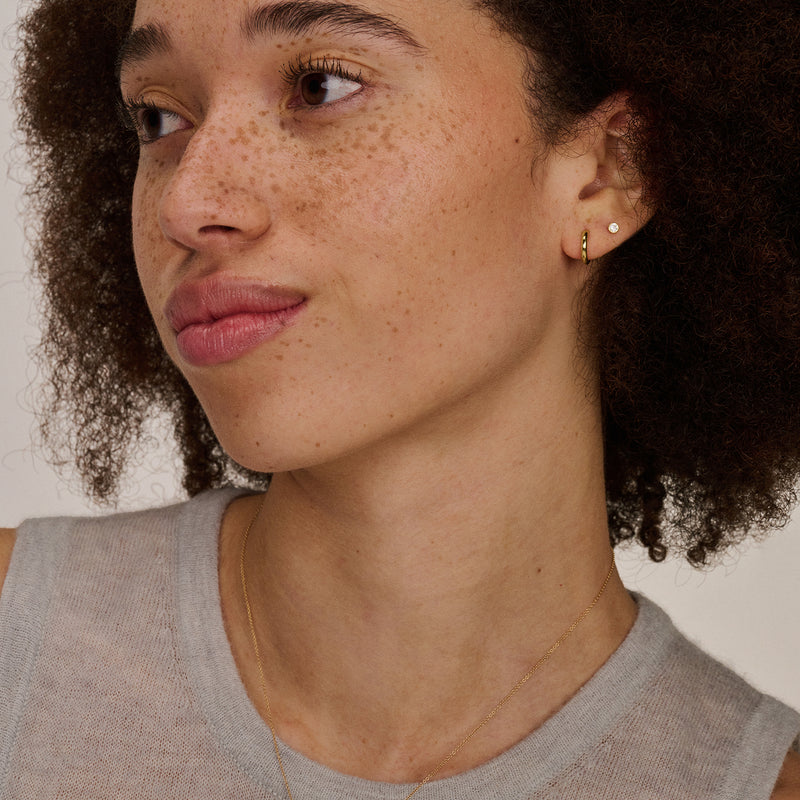 Oorknopje van 14k geelgoud met kleine heldere zirkonia steen, bicolor goud detail zichtbaar.