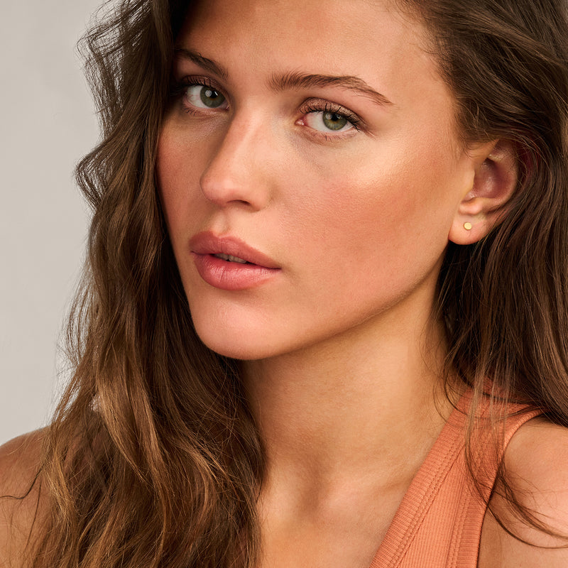 Kleine oorknopjes in 14k geelgoud gedragen door model met lang haar.