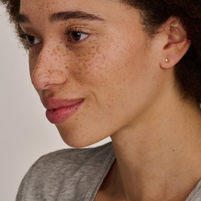 Puces d'oreilles en or 14k de forme ronde et lisse, portées à l'oreille gauche.