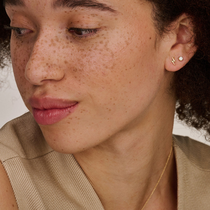 14k goud oorknop met zirkonia in zachte glans op oor van vrouw.