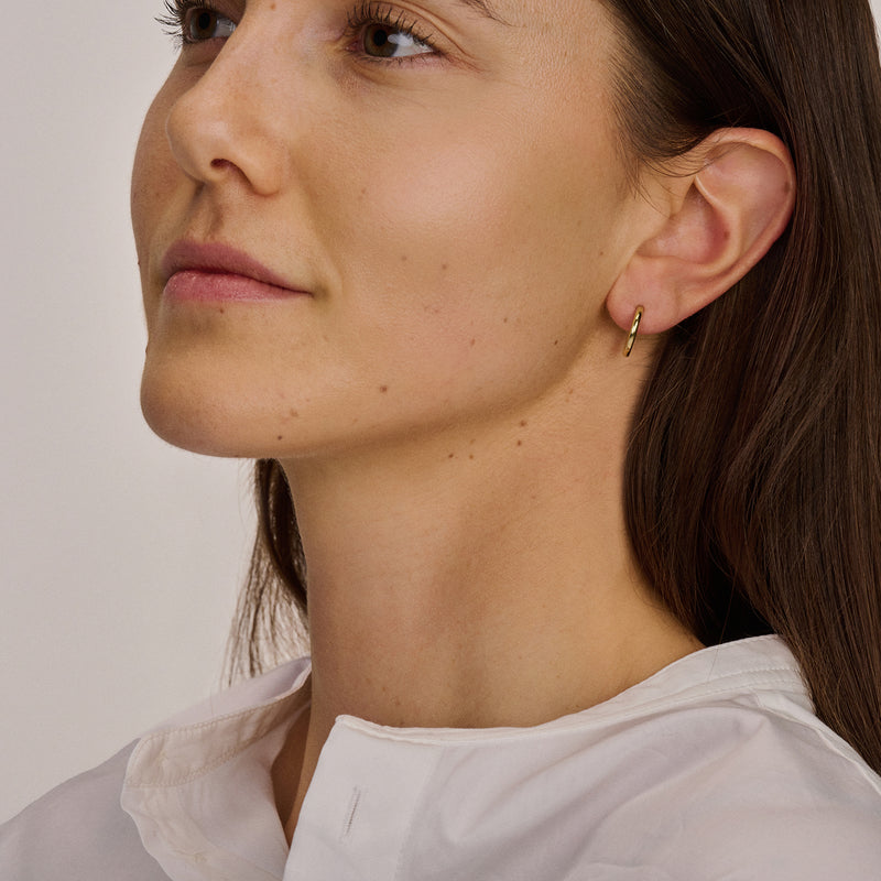 Oorringen van 14k geel goud subtiel gedragen in oor met gladde, ronde vorm.