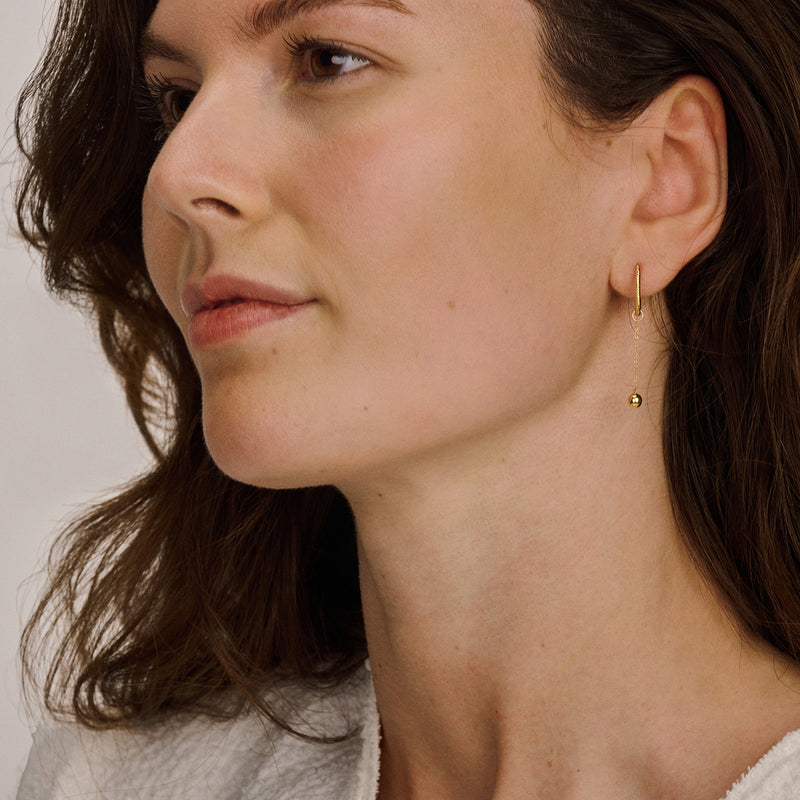 Oorring van 14k geelgoud met kleine hanger aan oorlel, bicolor goud effect zichtbaar.