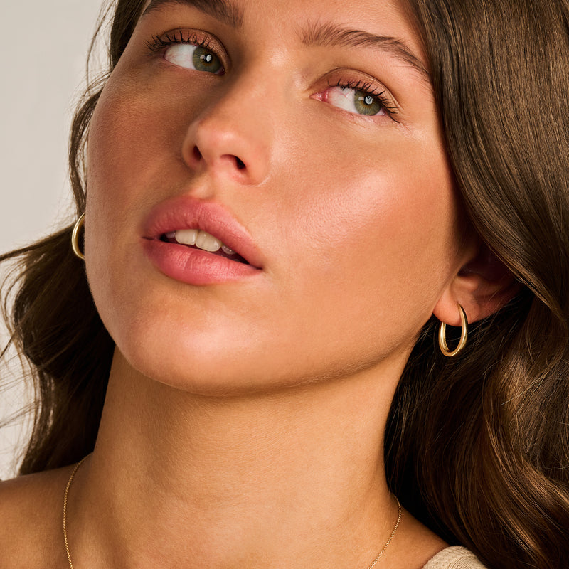 Oorringen van 14k geelgoud kleine creolen dicht bij het oor.