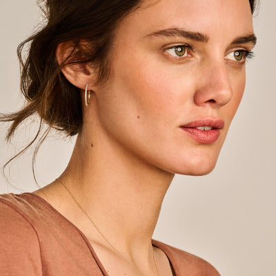 Oorring in 14k geelgoud met kleine zirkonia sluiting zichtbaar aan oor.