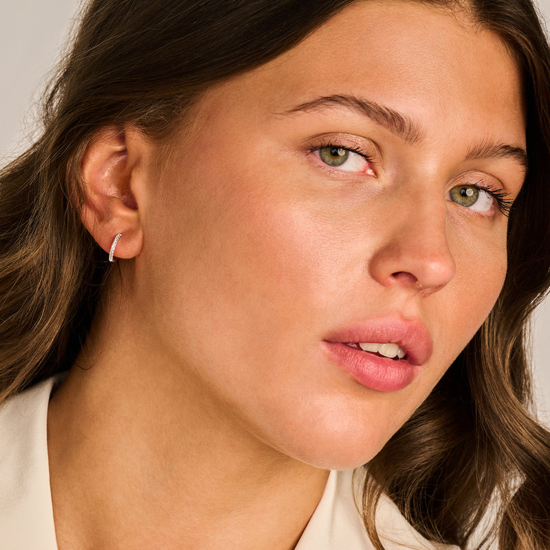 14k witgouden oorring met kleine zirkonia steentjes aan het oor van vrouw.