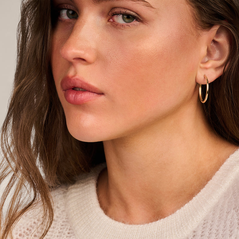 Oorring van 14k geelgoud, glad en rond met een subtiele glans.