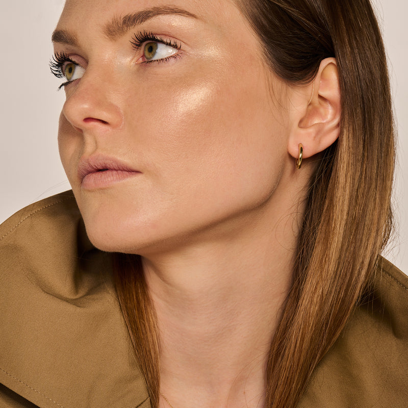 Oorringen van 14k geelgoud, klein en halfrond, gedragen door vrouw met lichtbruine haren.