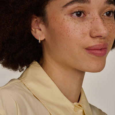 Oorringen van 14k geelgoud met glanzende zirkonia aan oor van vrouw.