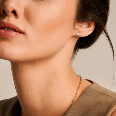 Kleine oorknop van 14k geelgoud gedragen aan oor, zachte glans, ronde vorm.