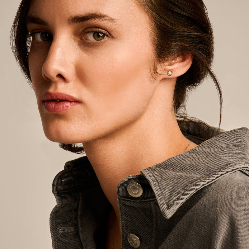 Clous d'oreilles en or 14k visibles sur le gros plan de l'oreille et de la peau claire au pelage gris.