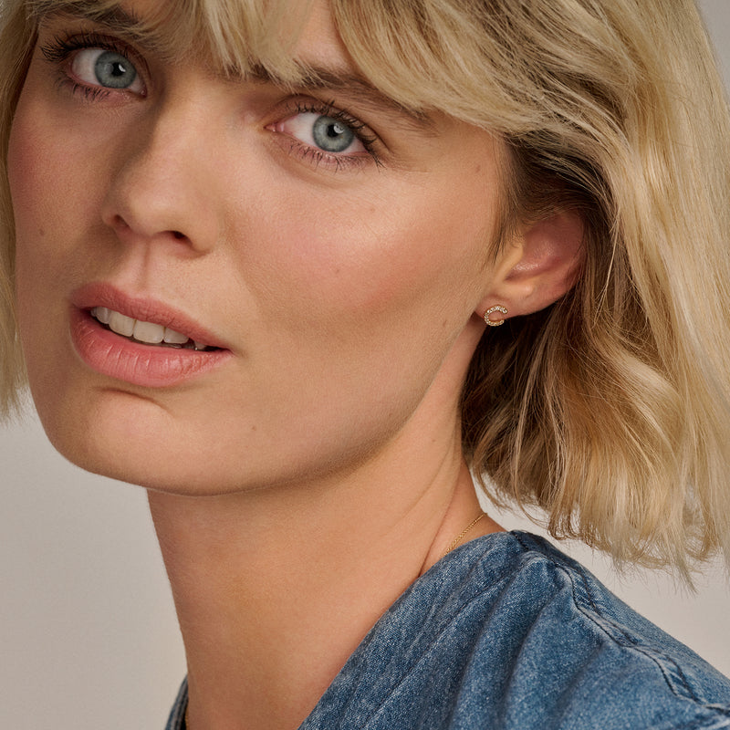 Oorknopjes 14k goud met glanzende zirkonia op oor van vrouw met blond haar.