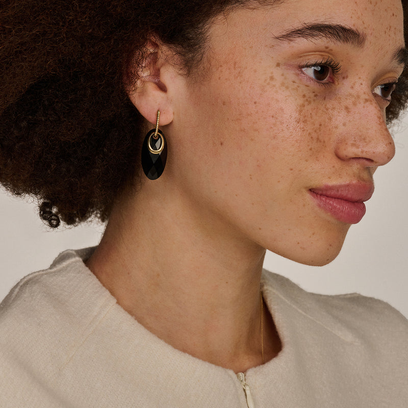 Oorring met bicolor 14k goud en zwart hangend element getragen door vrouw.