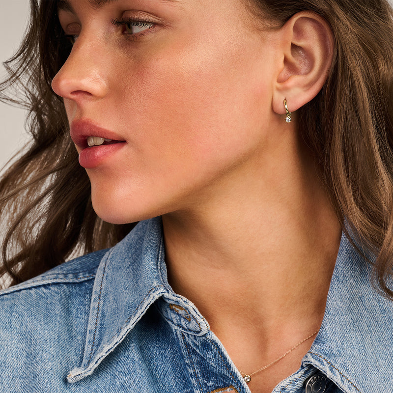 Breloques d'oreilles en or jaune 14k avec Zircone étincelante, portées par une femme avec une veste en jean.