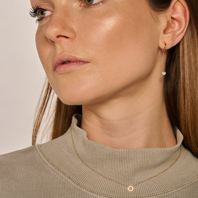 Oorbedel van 14k geelgoud met kleine zirkonia, gedragen aan oor van model.