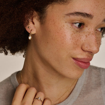 Puces d'oreilles en or jaune 14k avec pierre en perle sur l'oreille d'une femme aux cheveux bouclés.