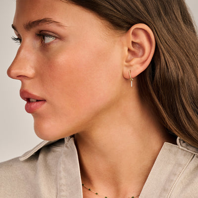 Oorbellen met kleine zirkonia in 14k geelgoud aan oor van vrouw.