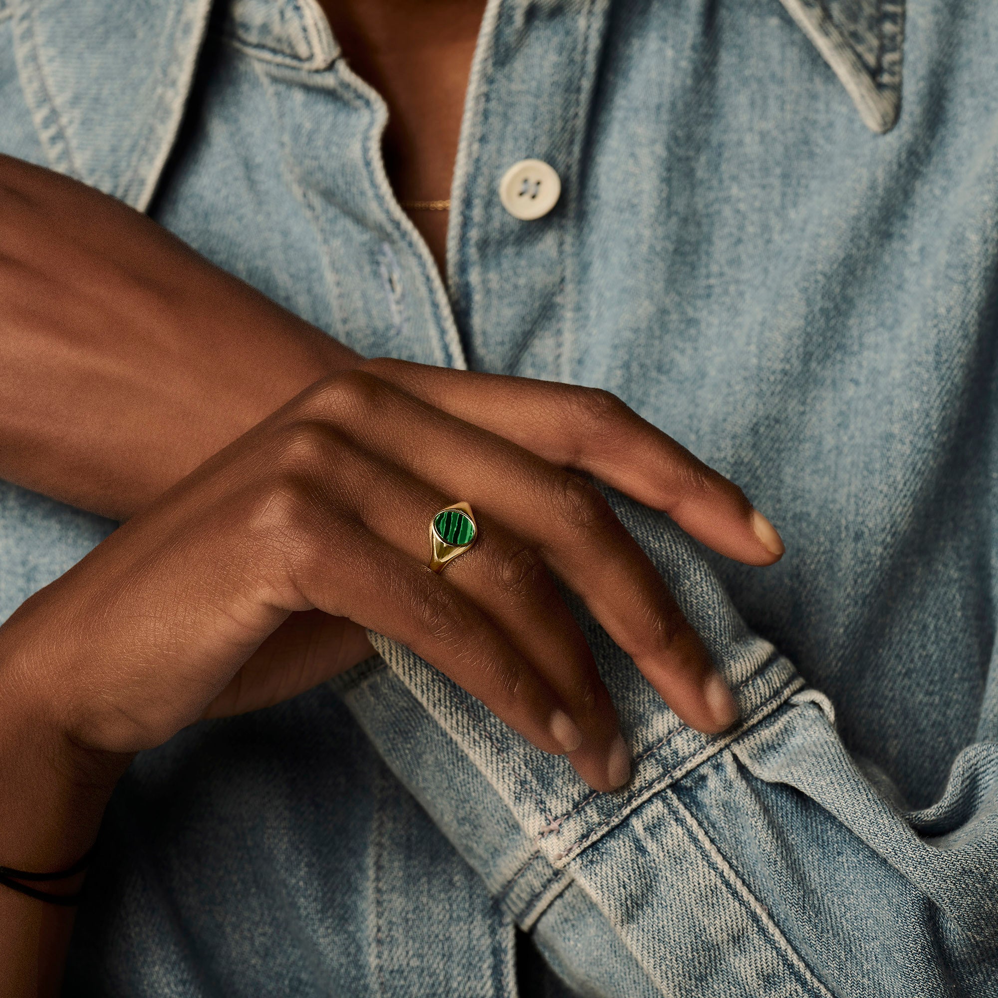 14k geelgouden zegelring met groene malachietsteen op donkere huid en denim blouse.