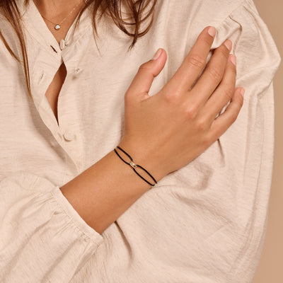 Armband van 14k geel goud met zwart zijdekoord aan damespols.