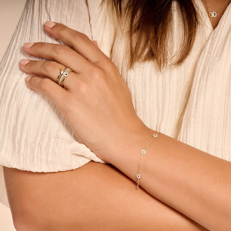14k geelgouden fijne schakelketting met zirkonia aan pols, gedragen bij lichte blouse.
