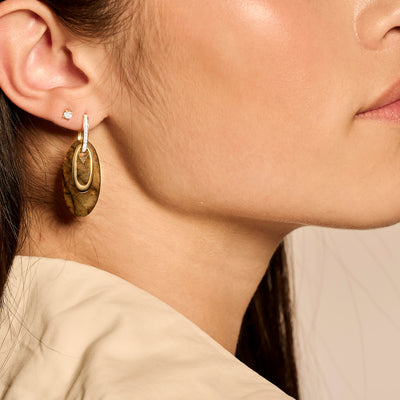 Oorknop met 14k geelgoud en kleine zirkonia aan oorlel, subtiel bicolor goud detail.