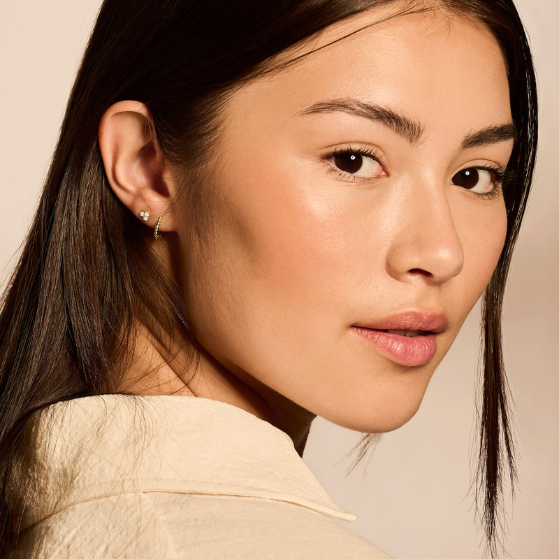 Ohrstecker aus 1485er Gelbgold mit kleinem Zirkonia im Ohr einer Frau mit braunem Haar.