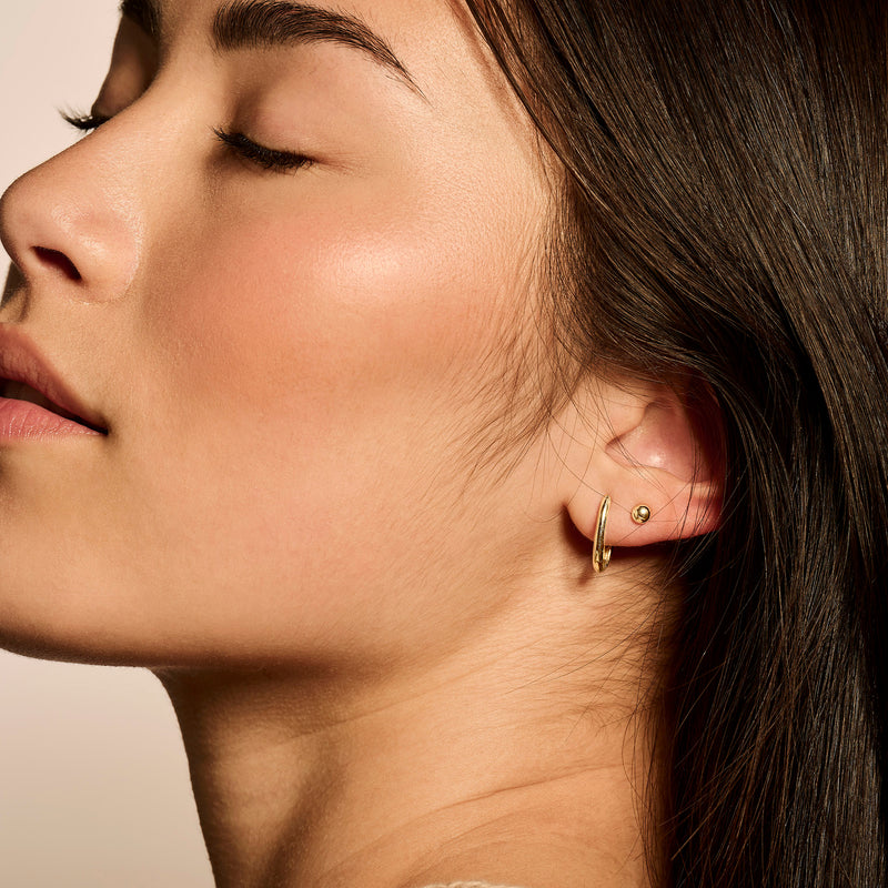 Oorring van 14k goud in eenvoudige halve cirkelvorm, gedragen aan vrouwelijke oorlel.
