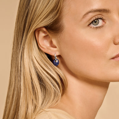 14k white gold earrings with pendant and dark blue gemstone in ear.