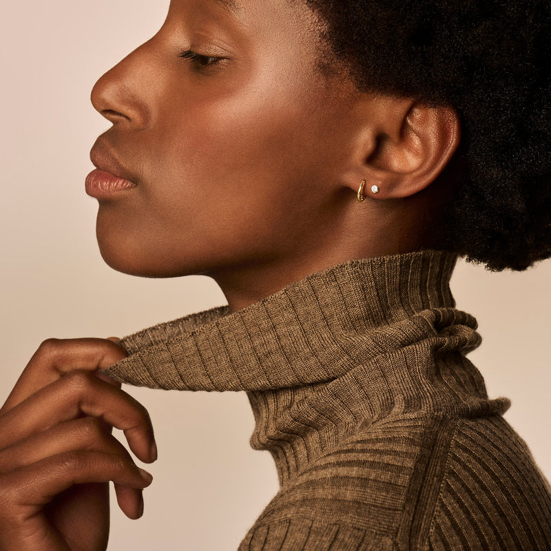 Ohrringe aus 585er Roségold mit subtilem Design, getragen von einer Frau mit braunem Rollkragenpullover.