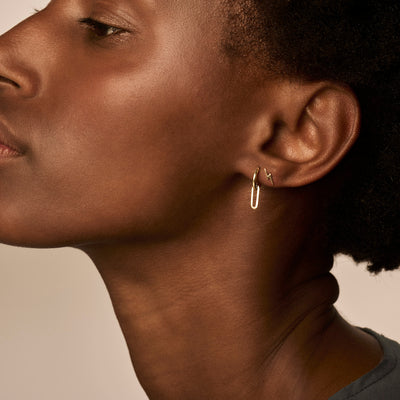 14k geelgouden oorring met slanke, minimalistische lusvorm, gedragen aan oorlel.