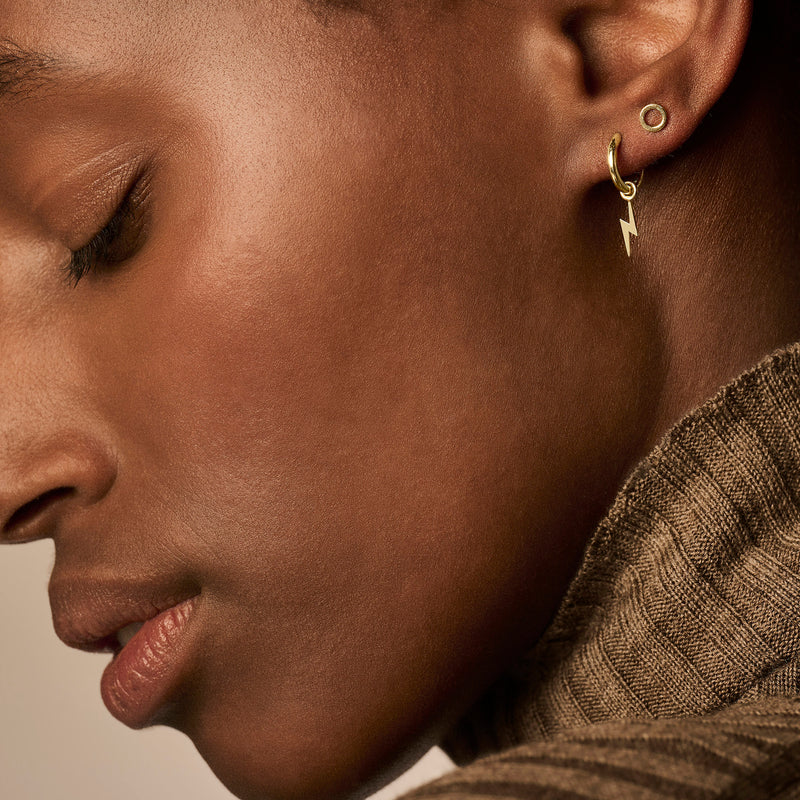 Puces d'oreilles en or jaune 14k avec un petit cercle et un pendentif en forme d'éclair à côté d'une boucle d'oreille roulée en or 14k.
